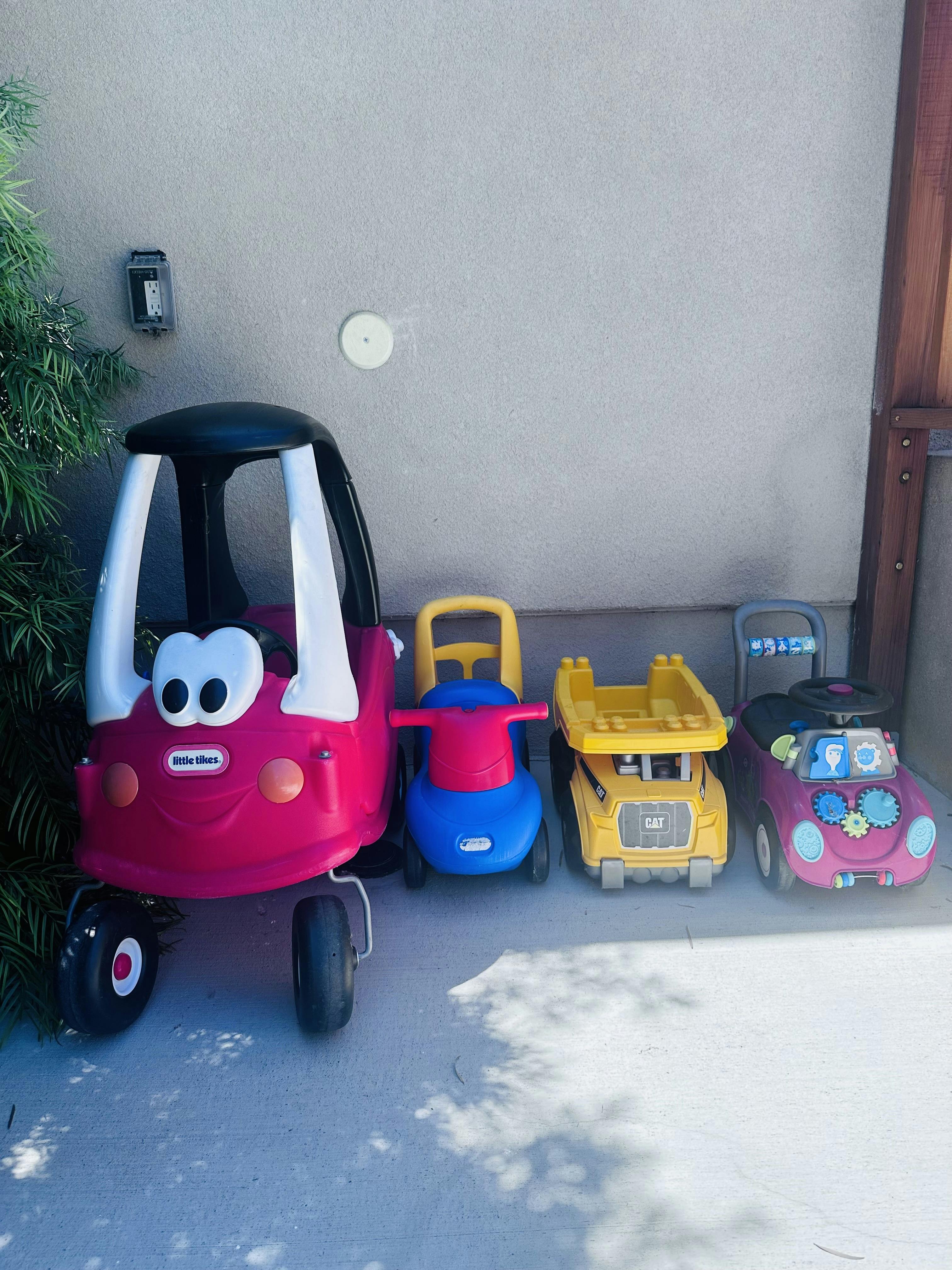 Four children's ride-on toy vehicles lined up against a wall