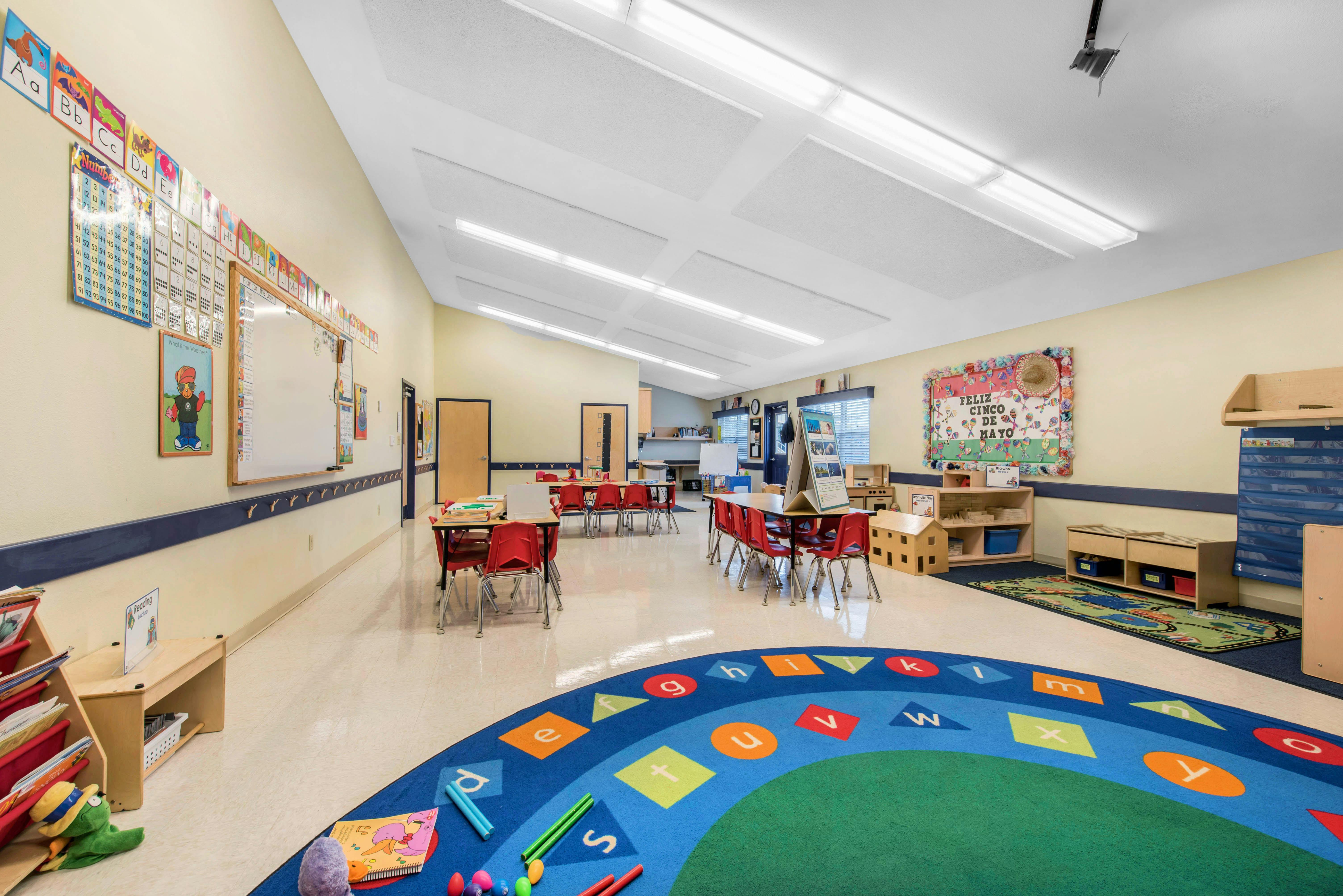 Classroom with tables, red chairs, and a blue alphabet rug