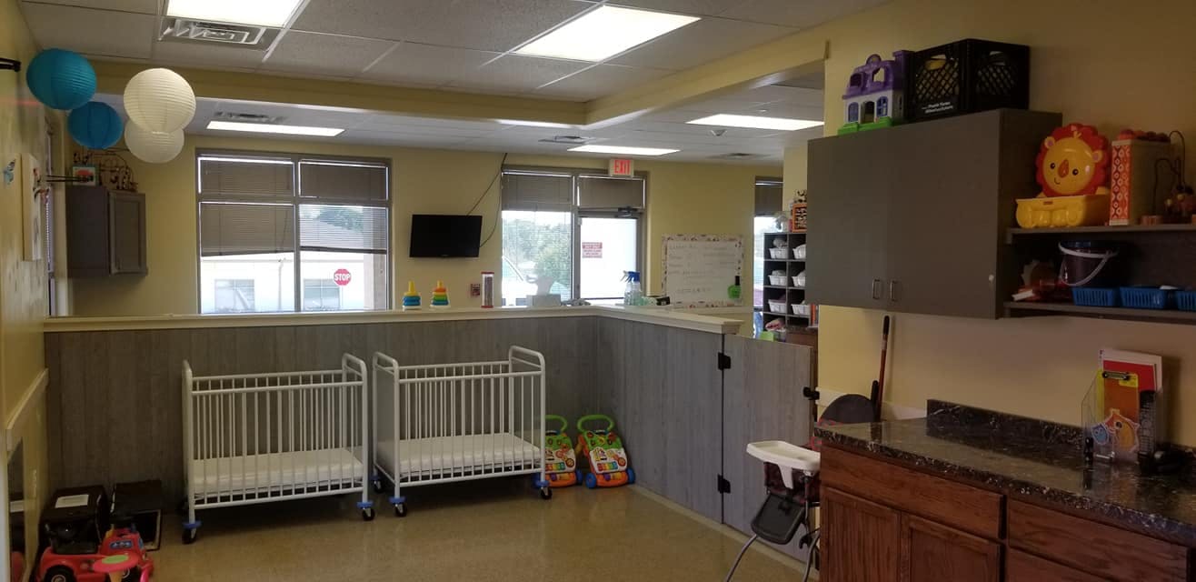 Two empty cribs in a room with windows and cabinets