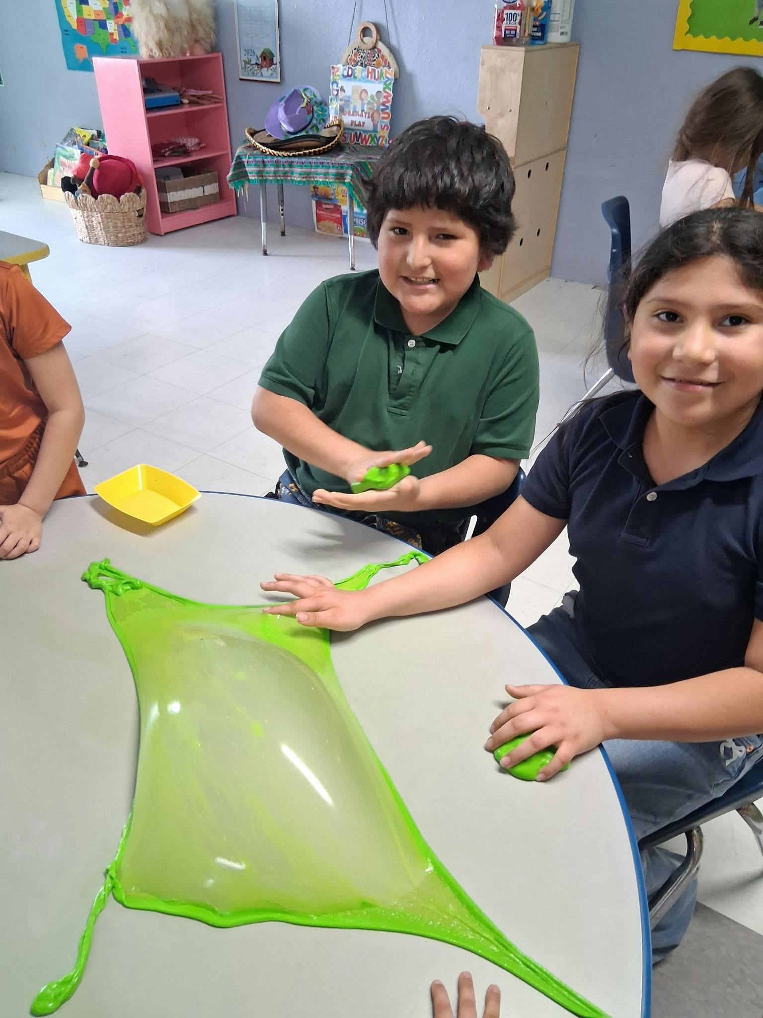 Children playing with green slime at a table in a classroom