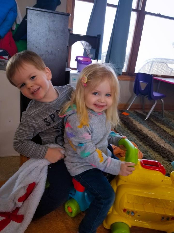 Two children, one sitting on a ride-on toy