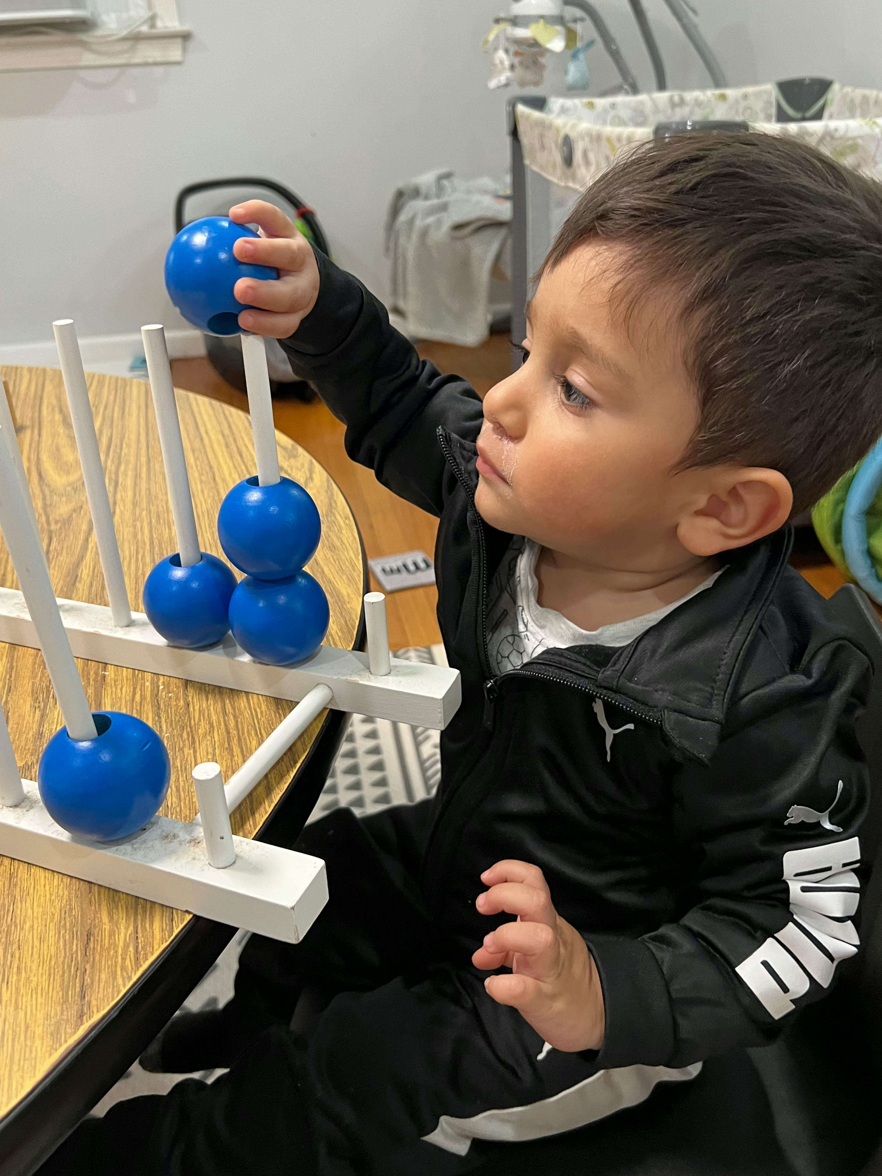 Child playing with a blue ball on a white peg toy