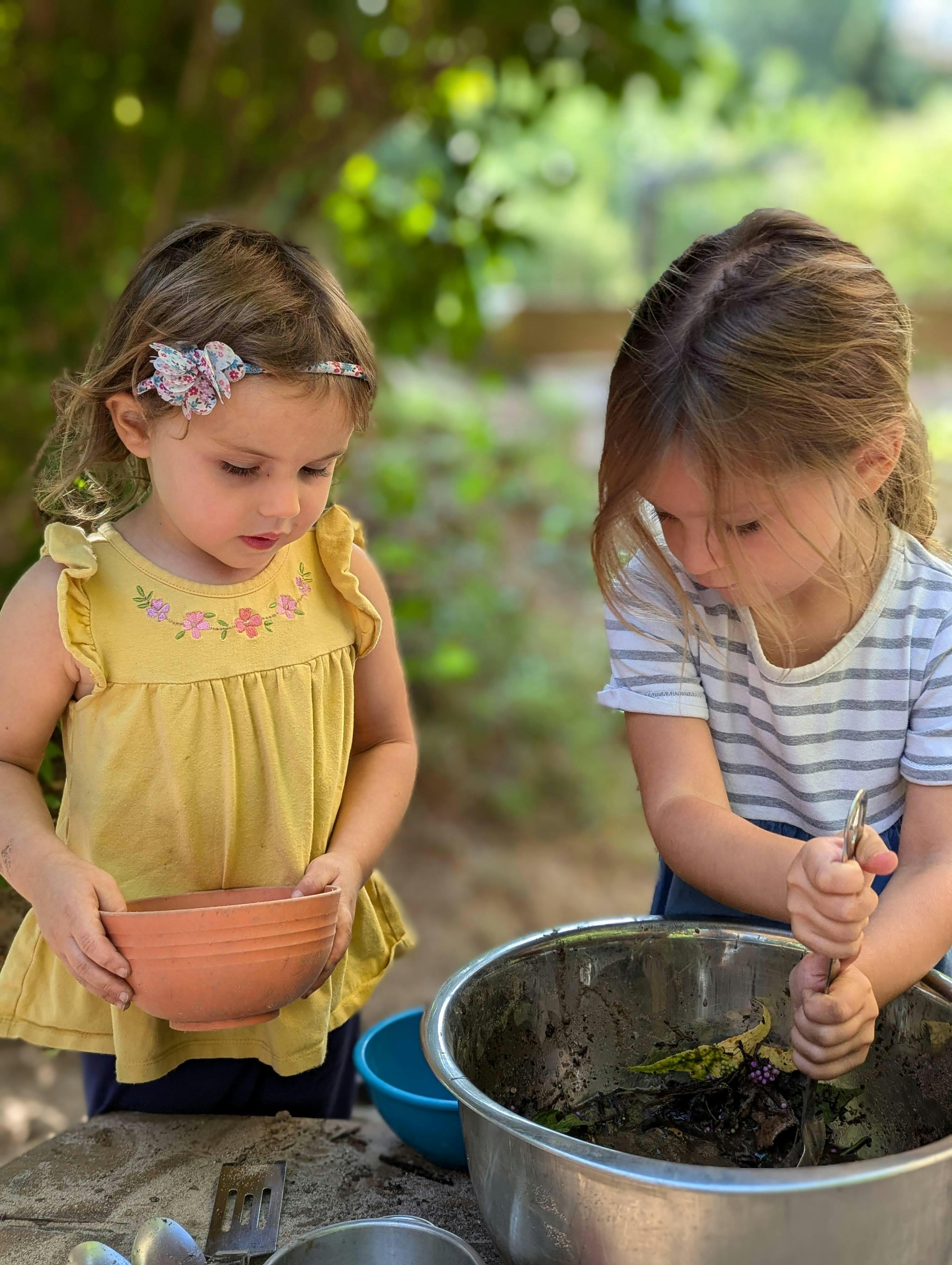 Two children playing with dirt and leaves in bowls