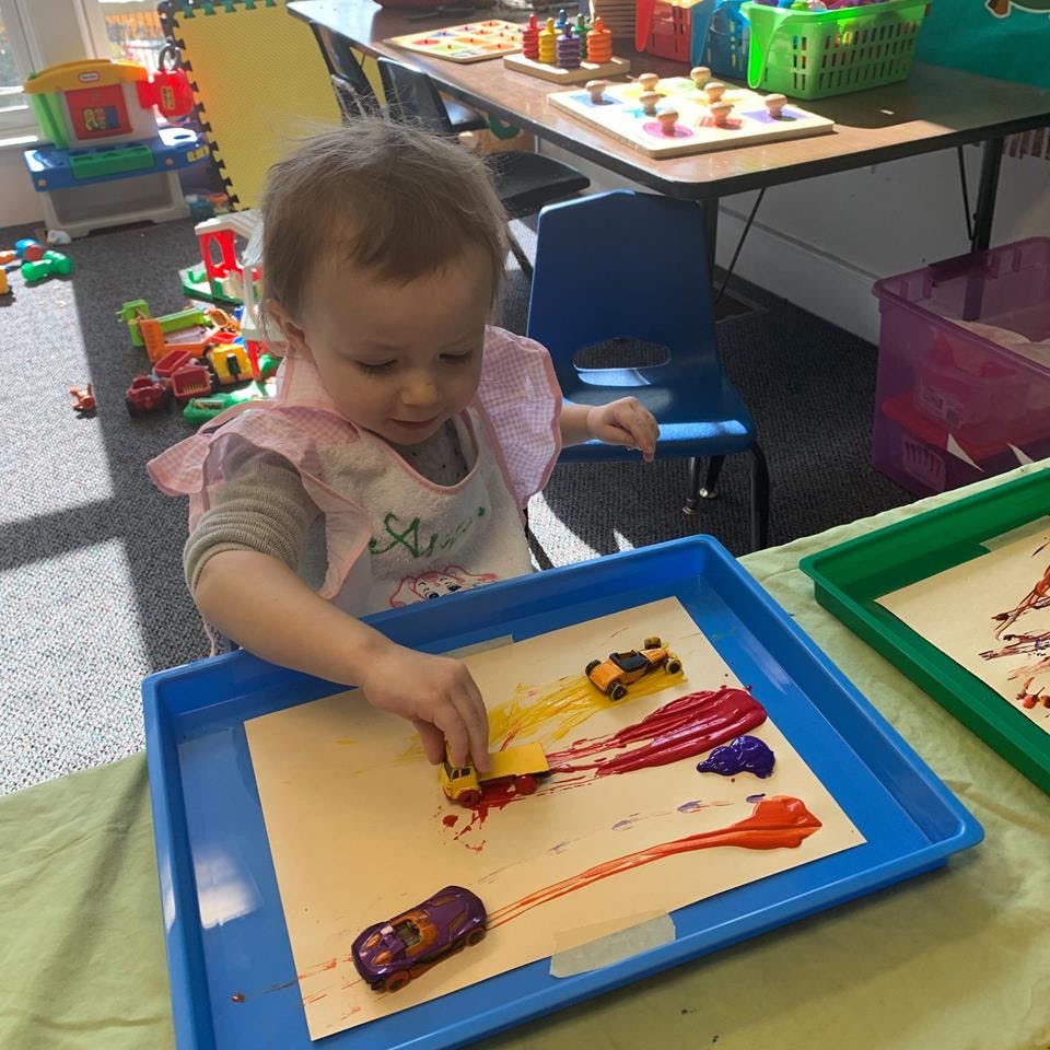 Child playing with toy cars and paint in a classroom