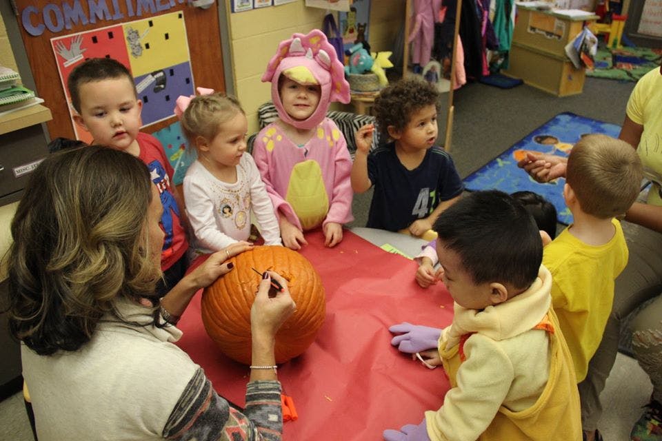 Adult and children gathered around a pumpkin on a red table