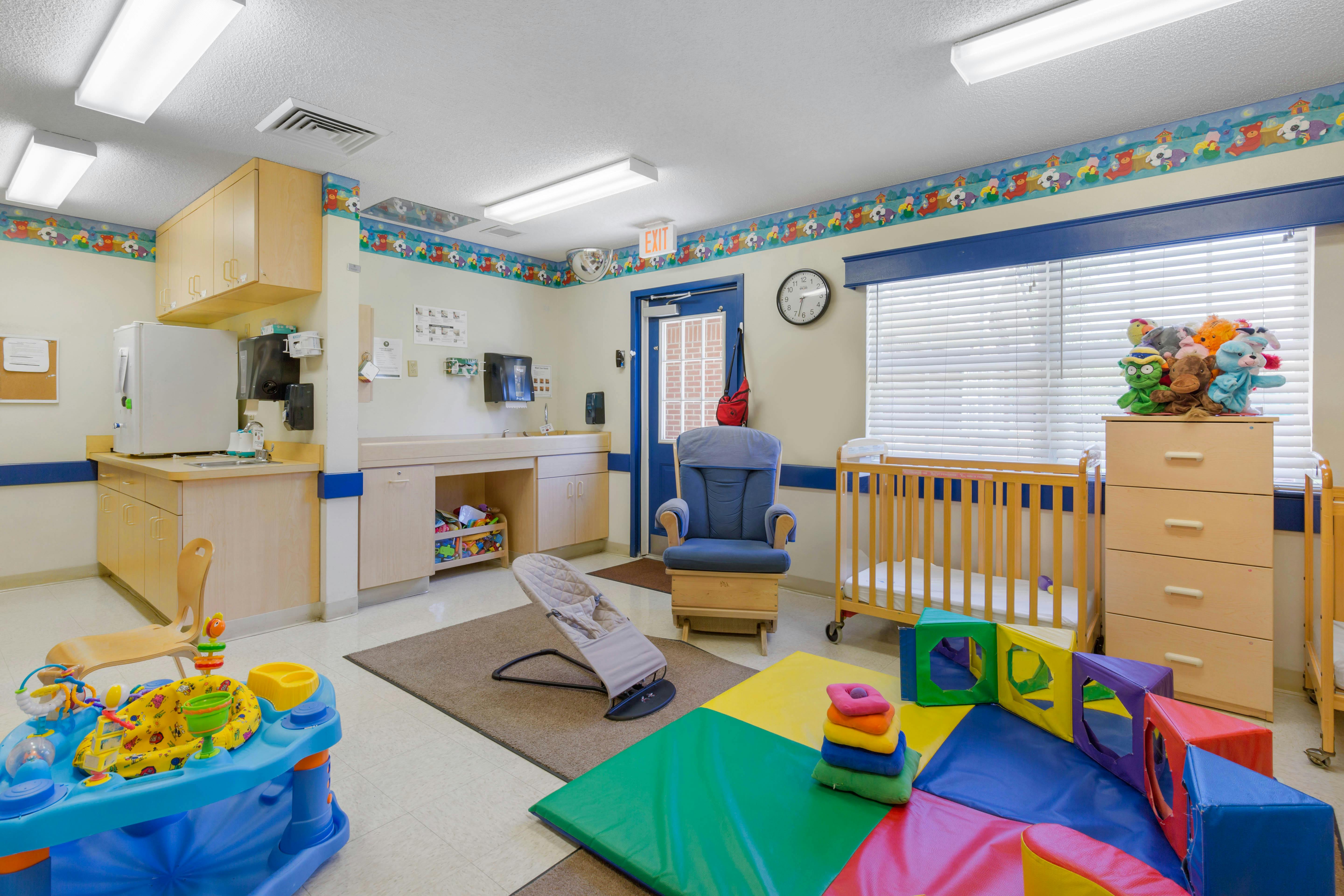 A colorful classroom with cribs, play mats, and a changing station