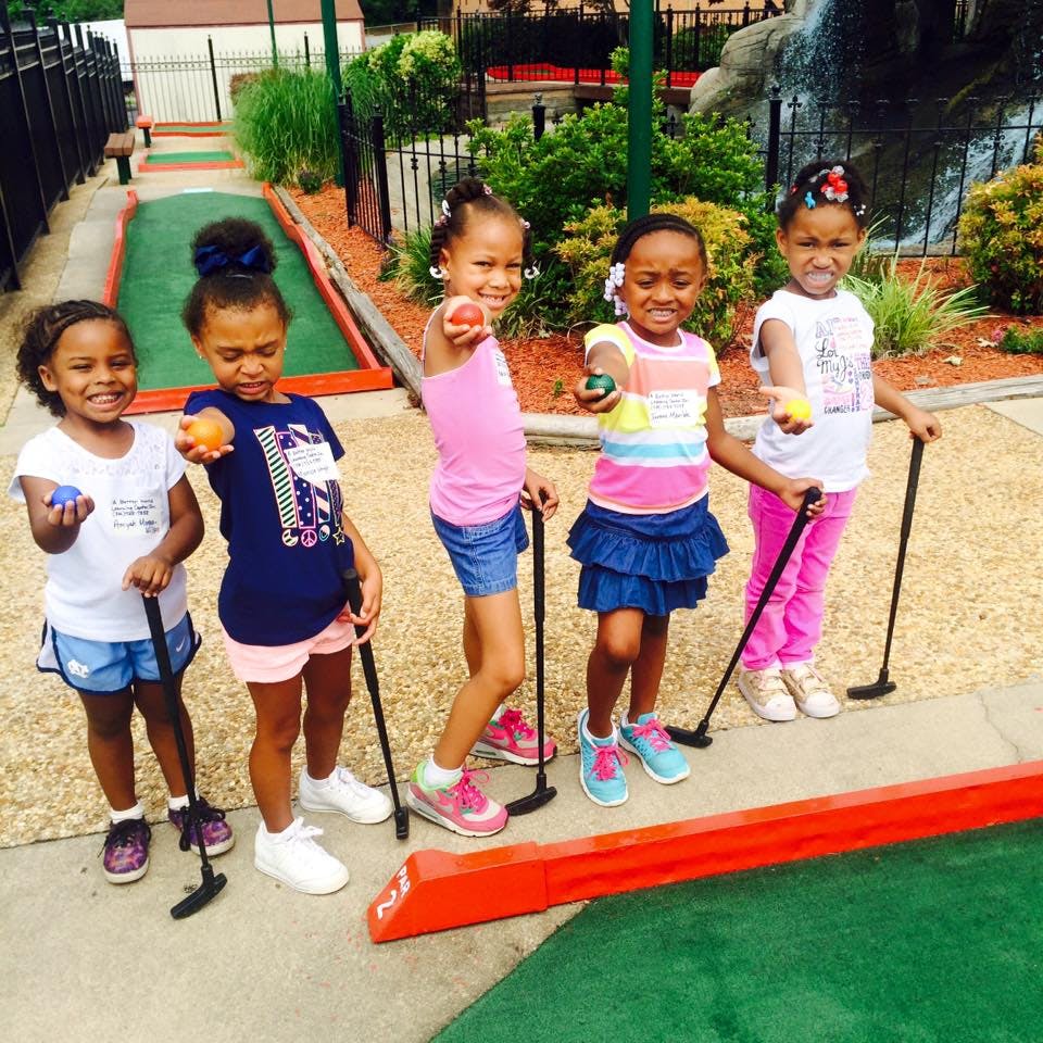 Five children holding golf clubs and balls on a miniature golf course