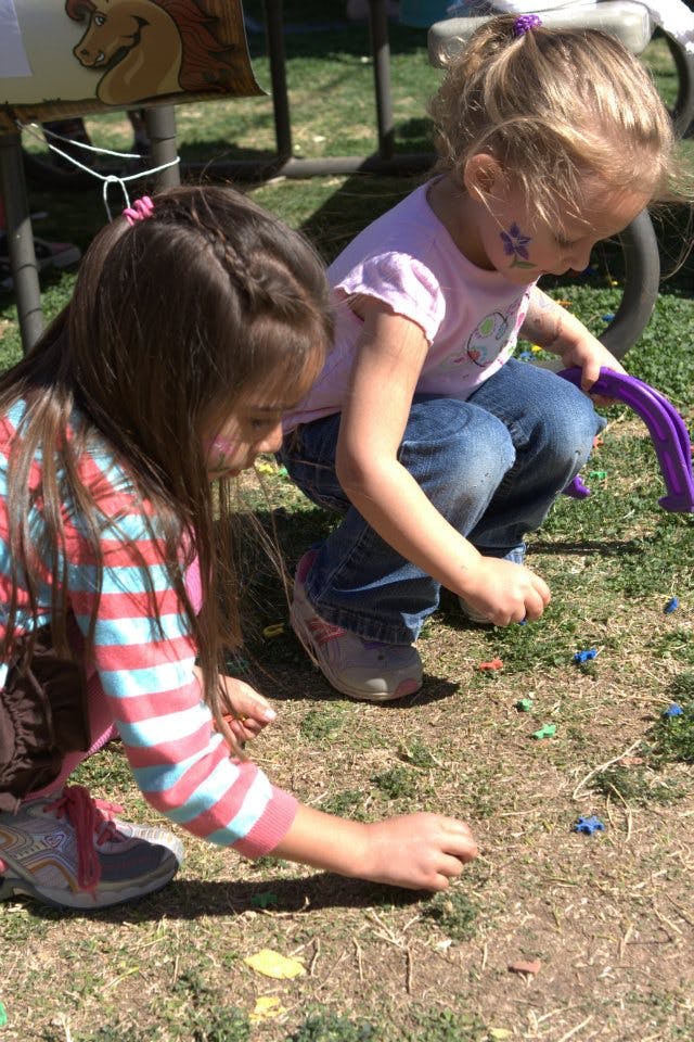 Two children crouching on grass picking up small objects