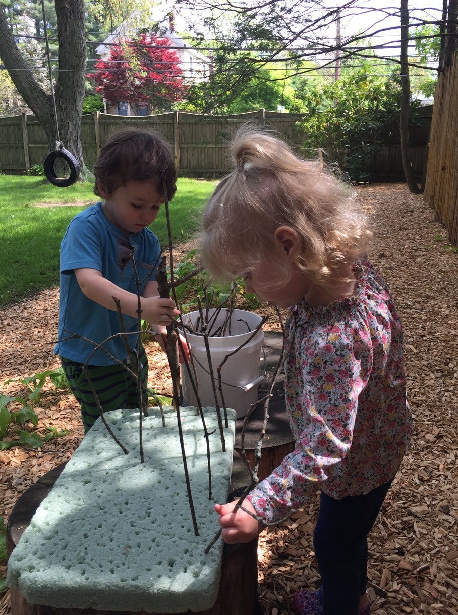 Two children playing with sticks and a foam block outdoors