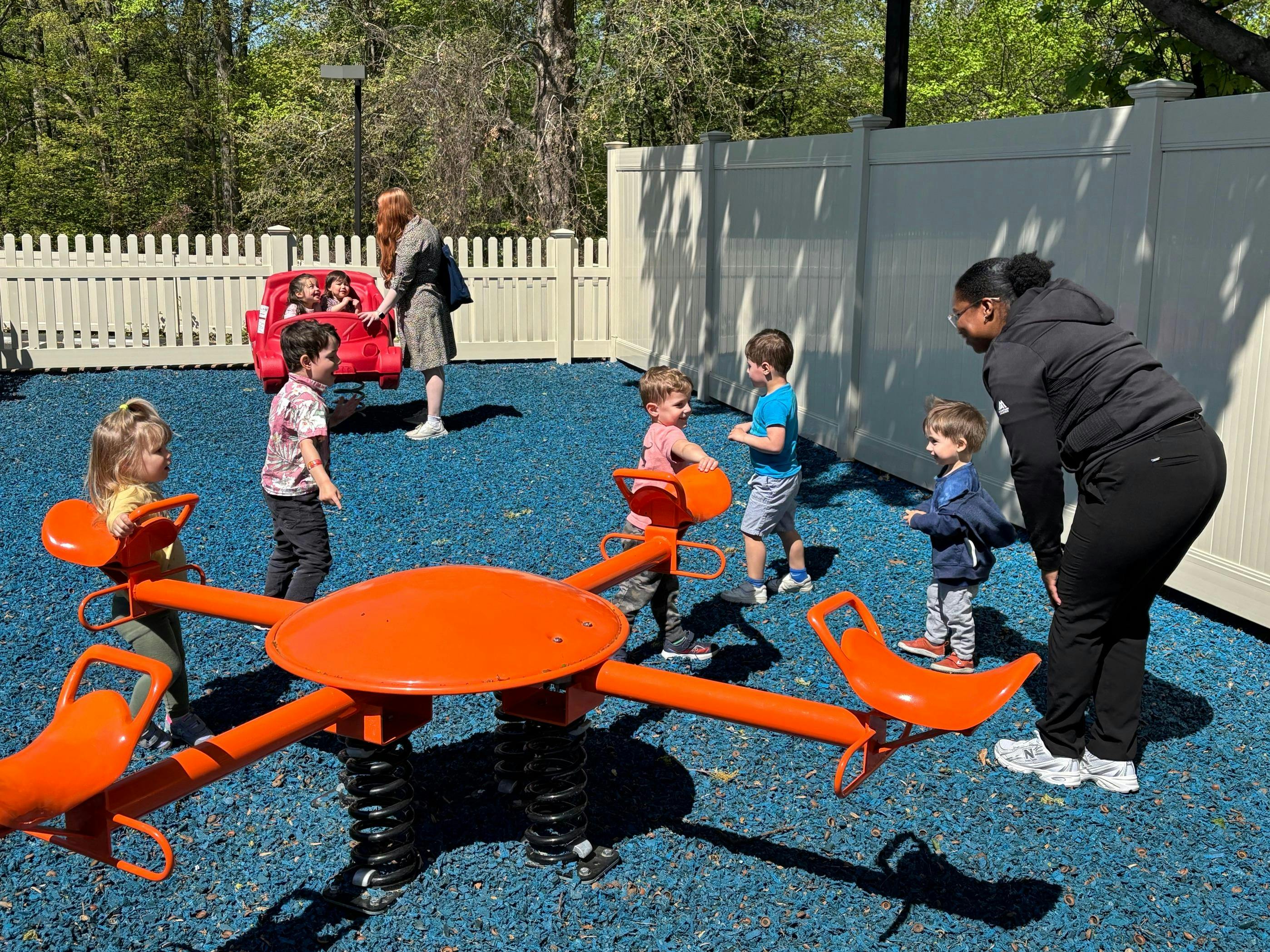 Adults supervising children playing on a playground with an orange seesaw