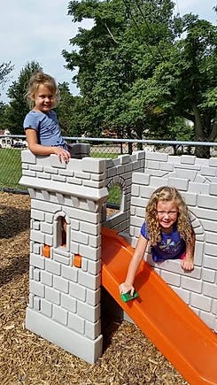 Two children playing on a castle-themed playground structure with a slide