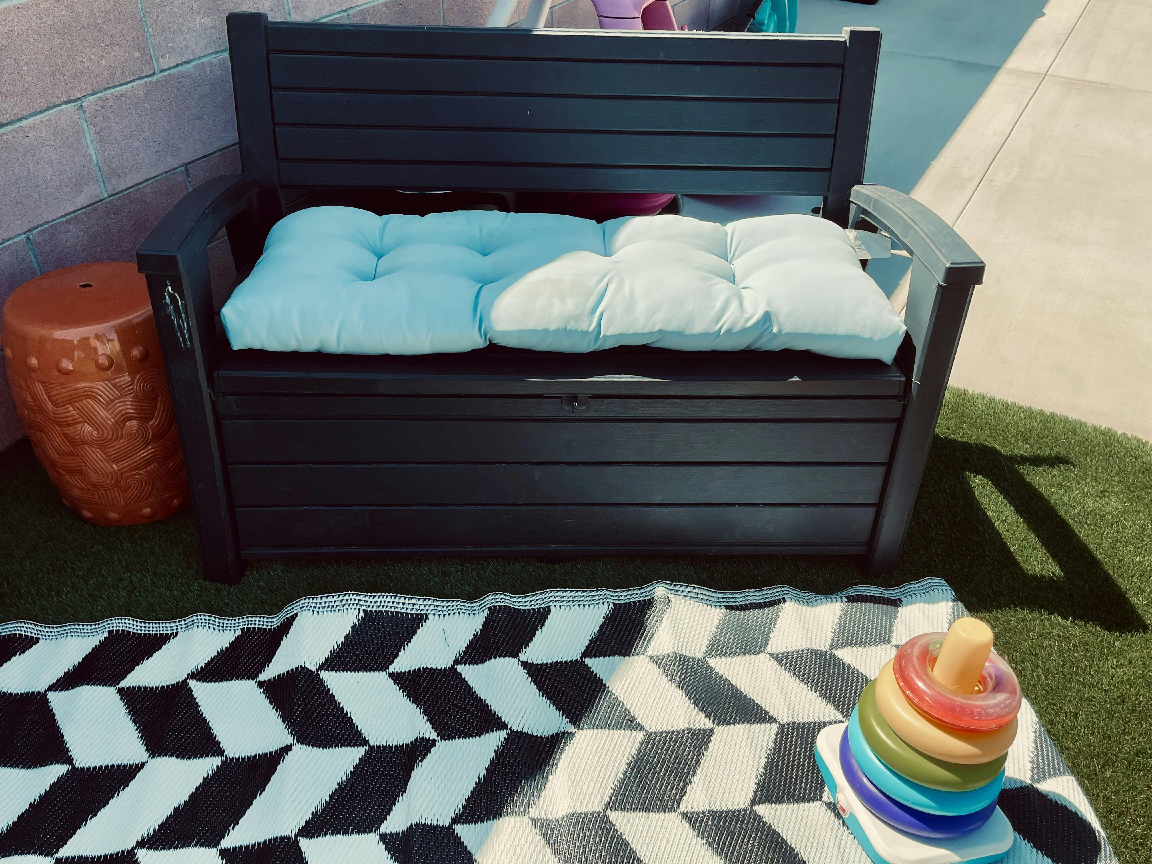 Outdoor storage bench with cushions, patterned rug, and stacking toy