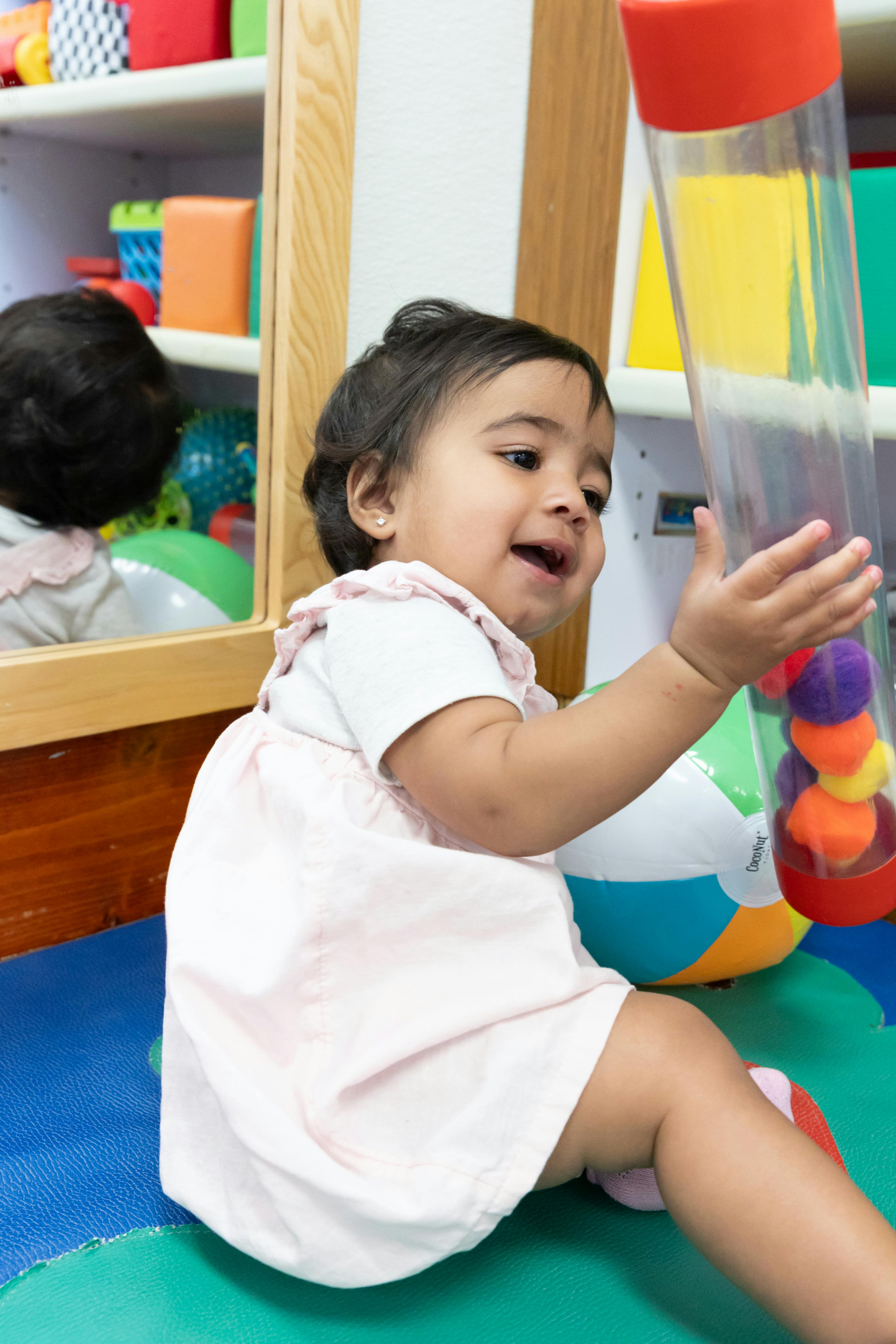 Child playing with a clear tube toy filled with colorful pom-poms