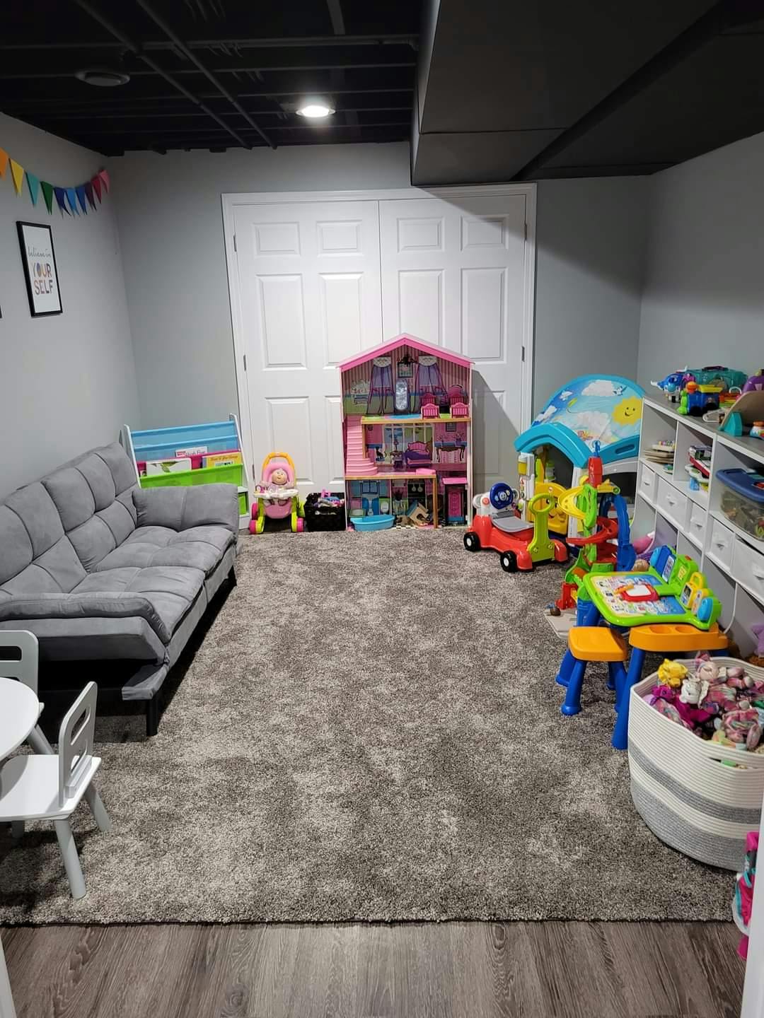 Playroom with a gray sofa, dollhouse, and various toys