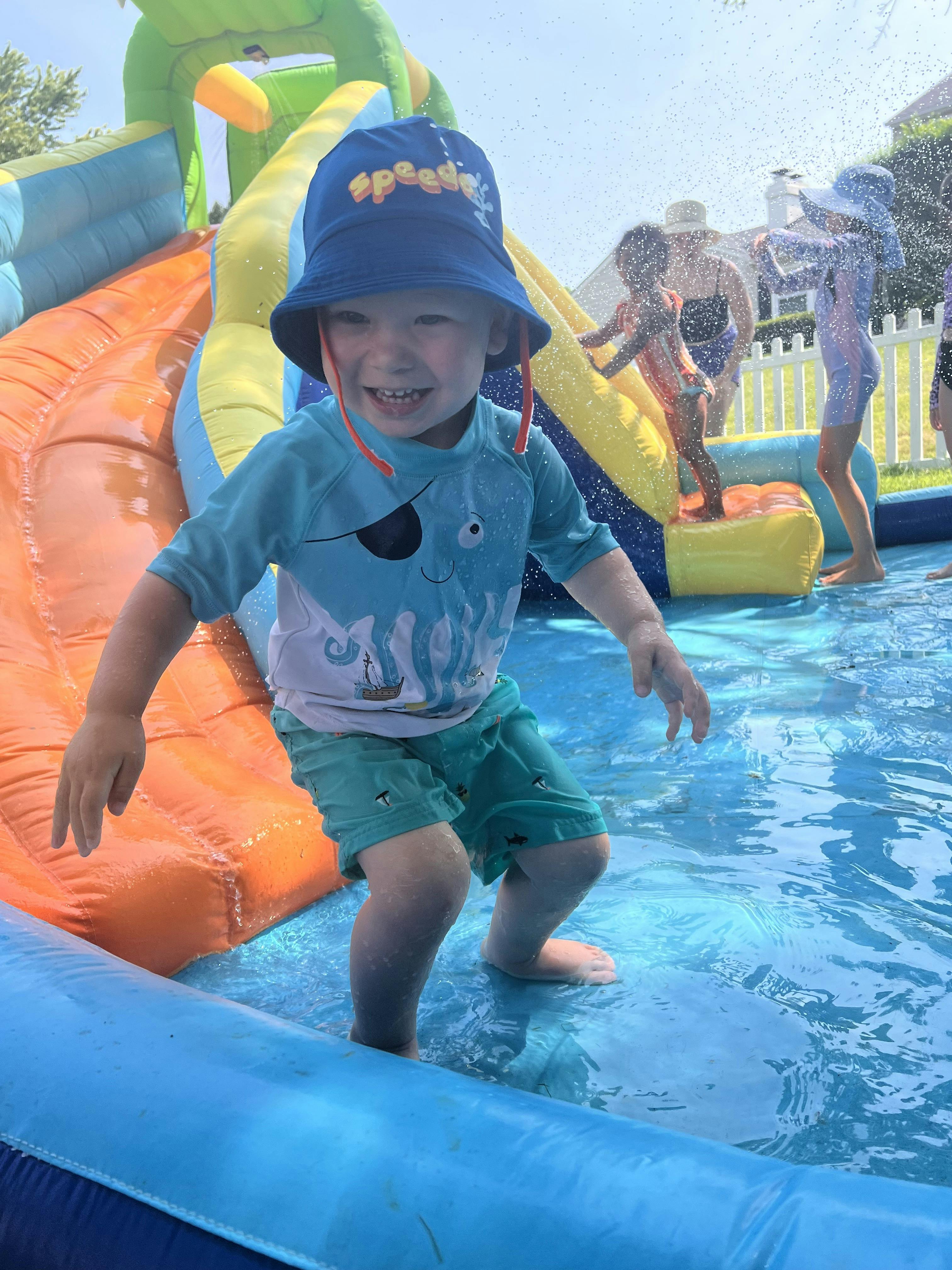 Child wearing a hat and swim gear playing in a water slide pool
