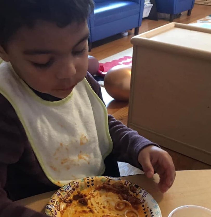 Child in a bib eating pasta from a paper plate