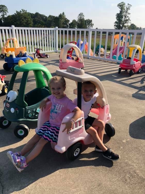 Two children sitting in toy cars on a playground