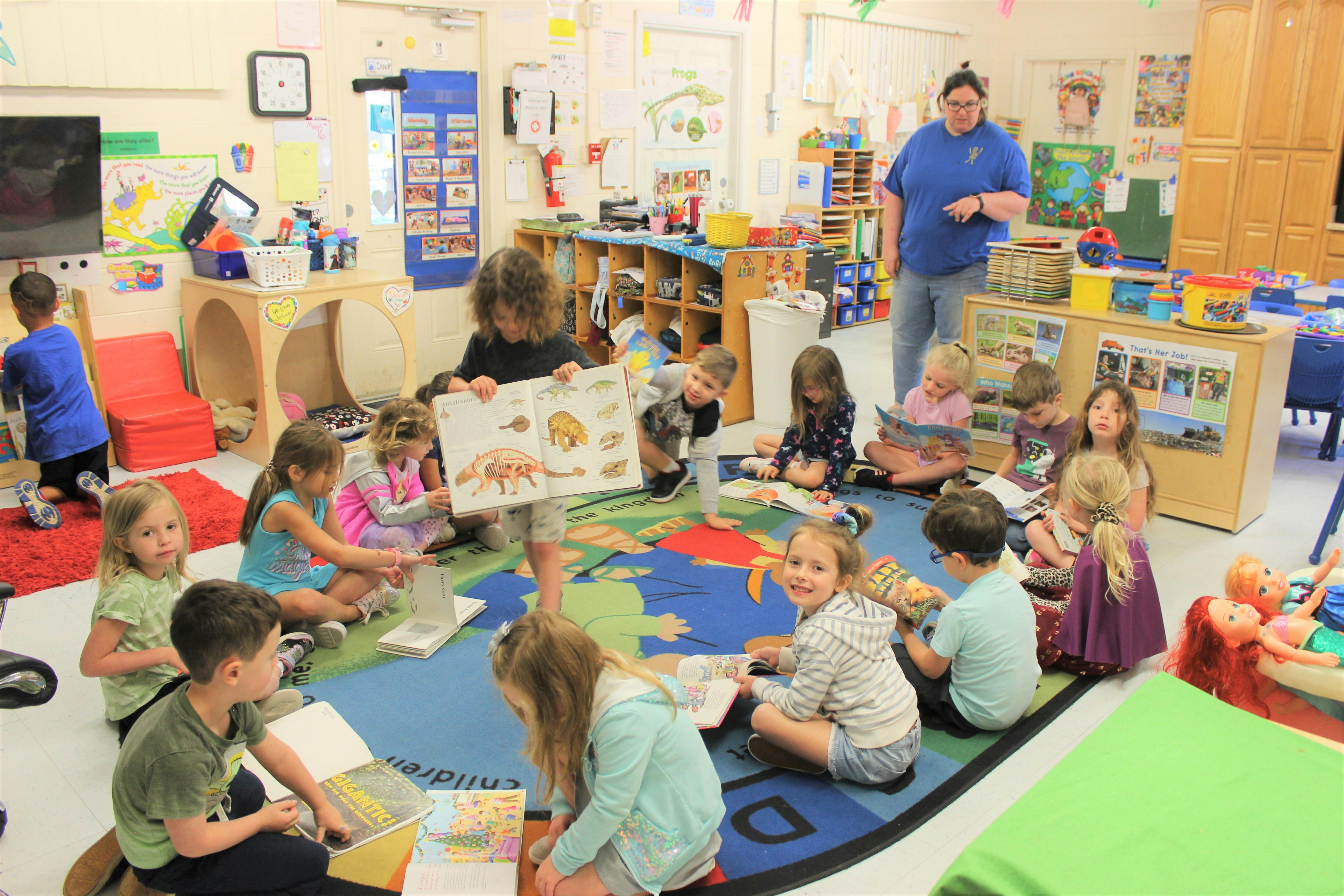 Children sitting on a rug in a classroom, one child holding up a book