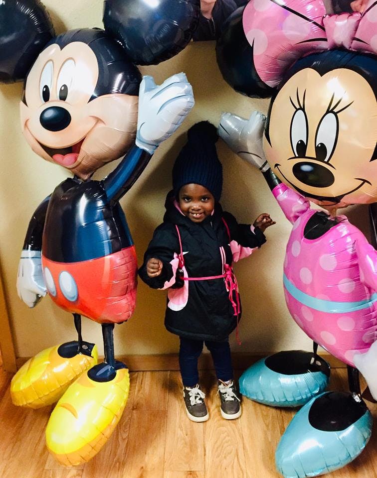 Child standing between large Mickey and Minnie Mouse balloons