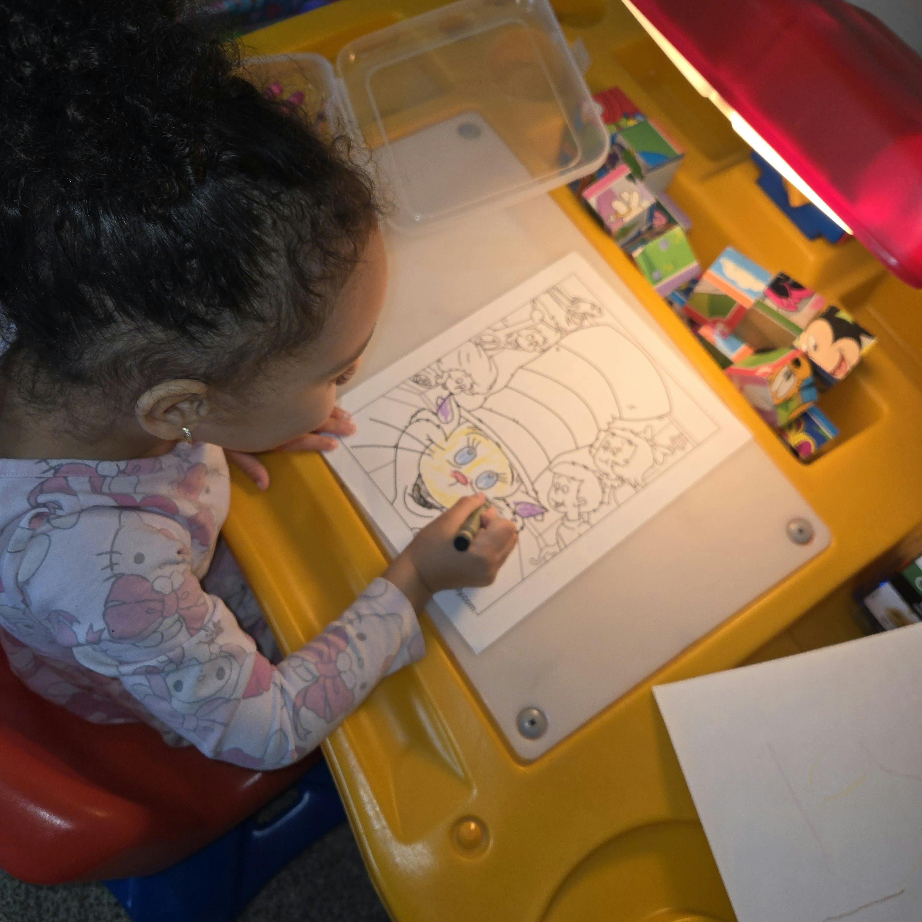 Child coloring a picture on a light table with a yellow crayon