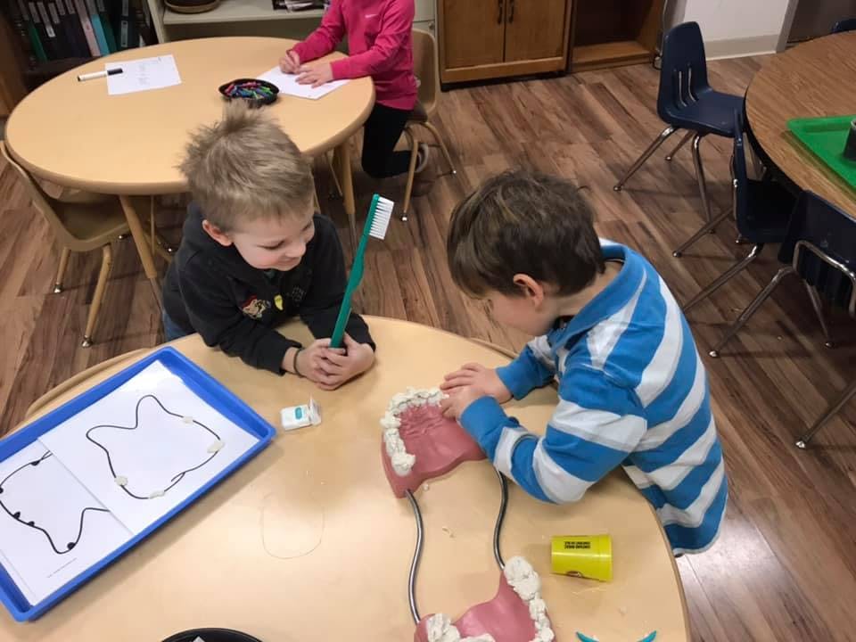 Two children at a table with a large dental model and a toothbrush