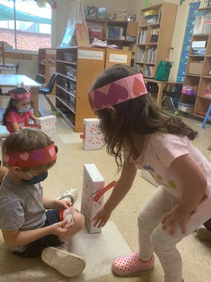 Children wearing heart headbands playing with white boxes in a classroom