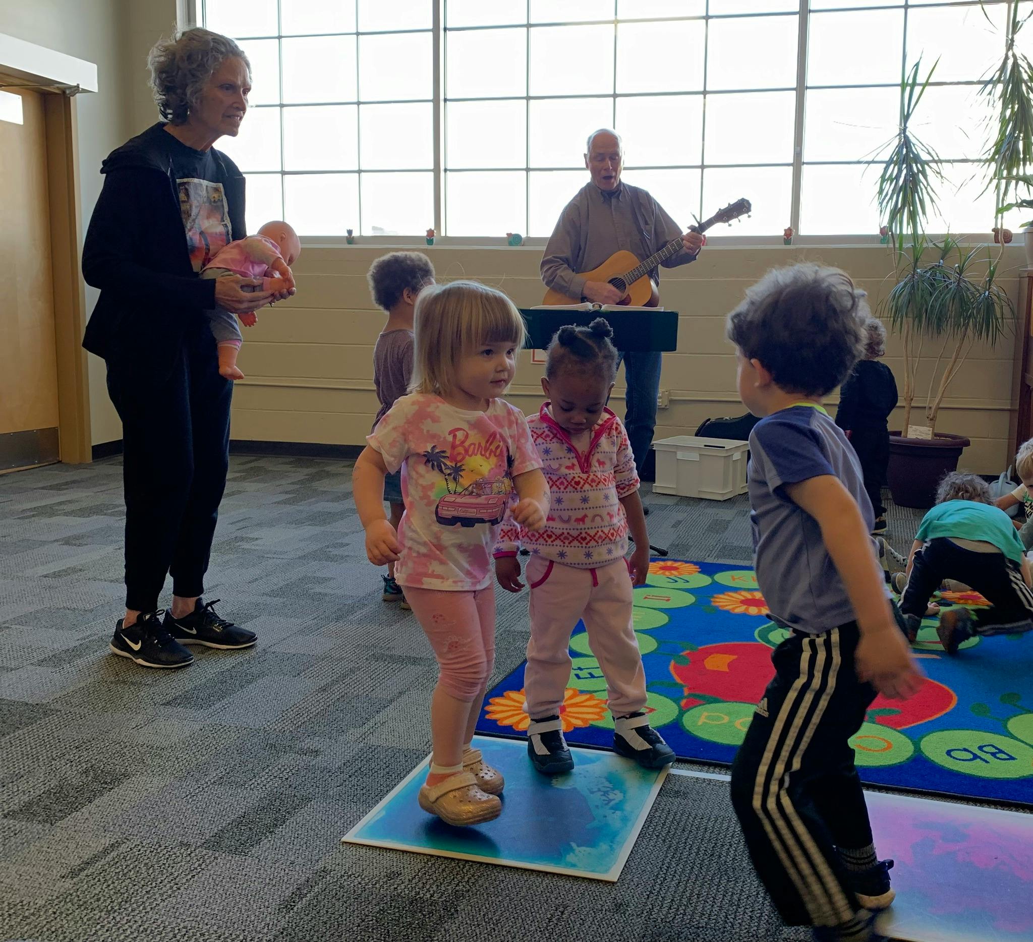Adults and children in a room, one adult playing guitar