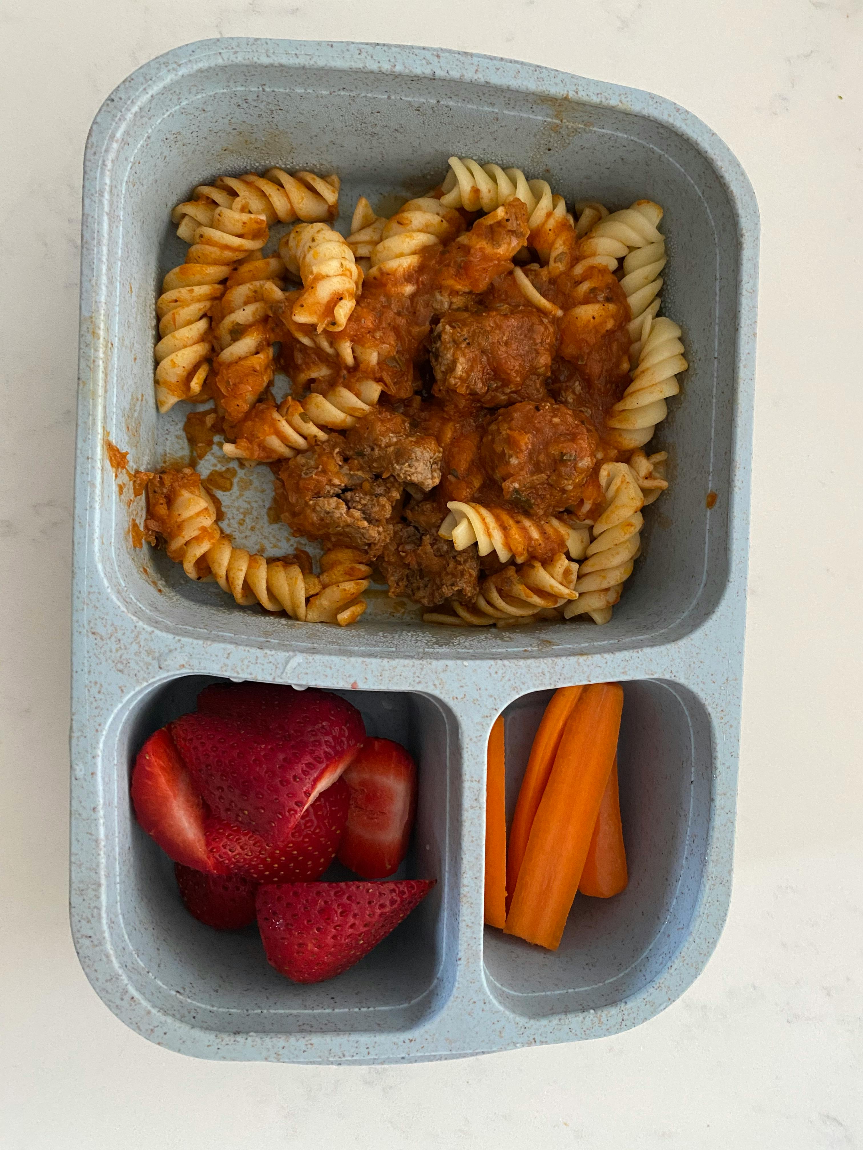 Pasta with meatballs, strawberries, and carrots in a divided container