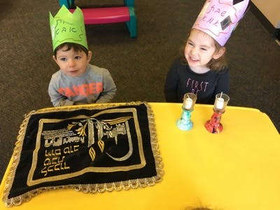 Two children wearing crowns at a table with a decorative cloth and candles