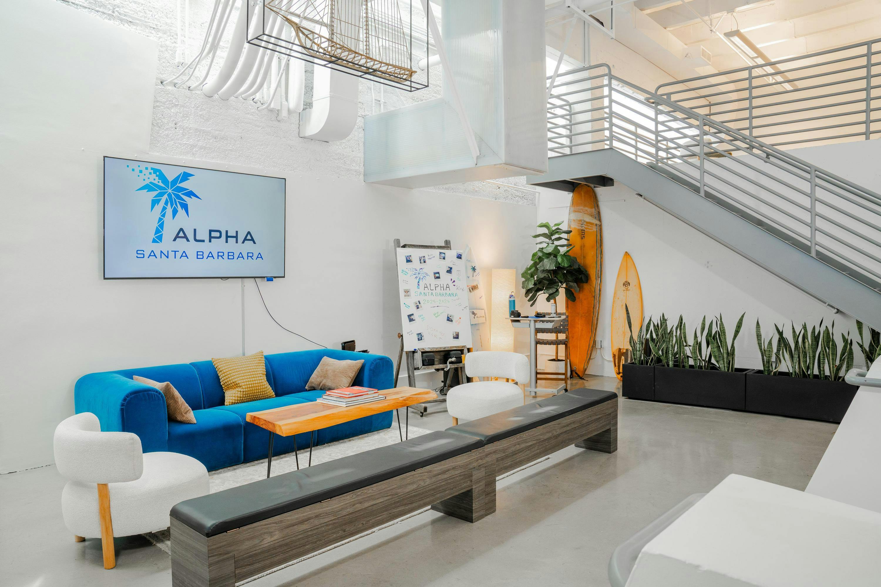 Lounge area with a blue couch, coffee table, white chairs, and a TV screen