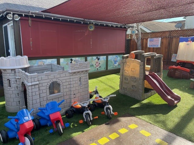 Outdoor play area with toy castle, slides, and tricycles on artificial grass