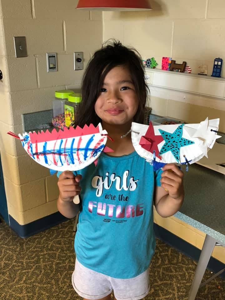 Child holding two paper plate crafts with red, white, and blue designs
