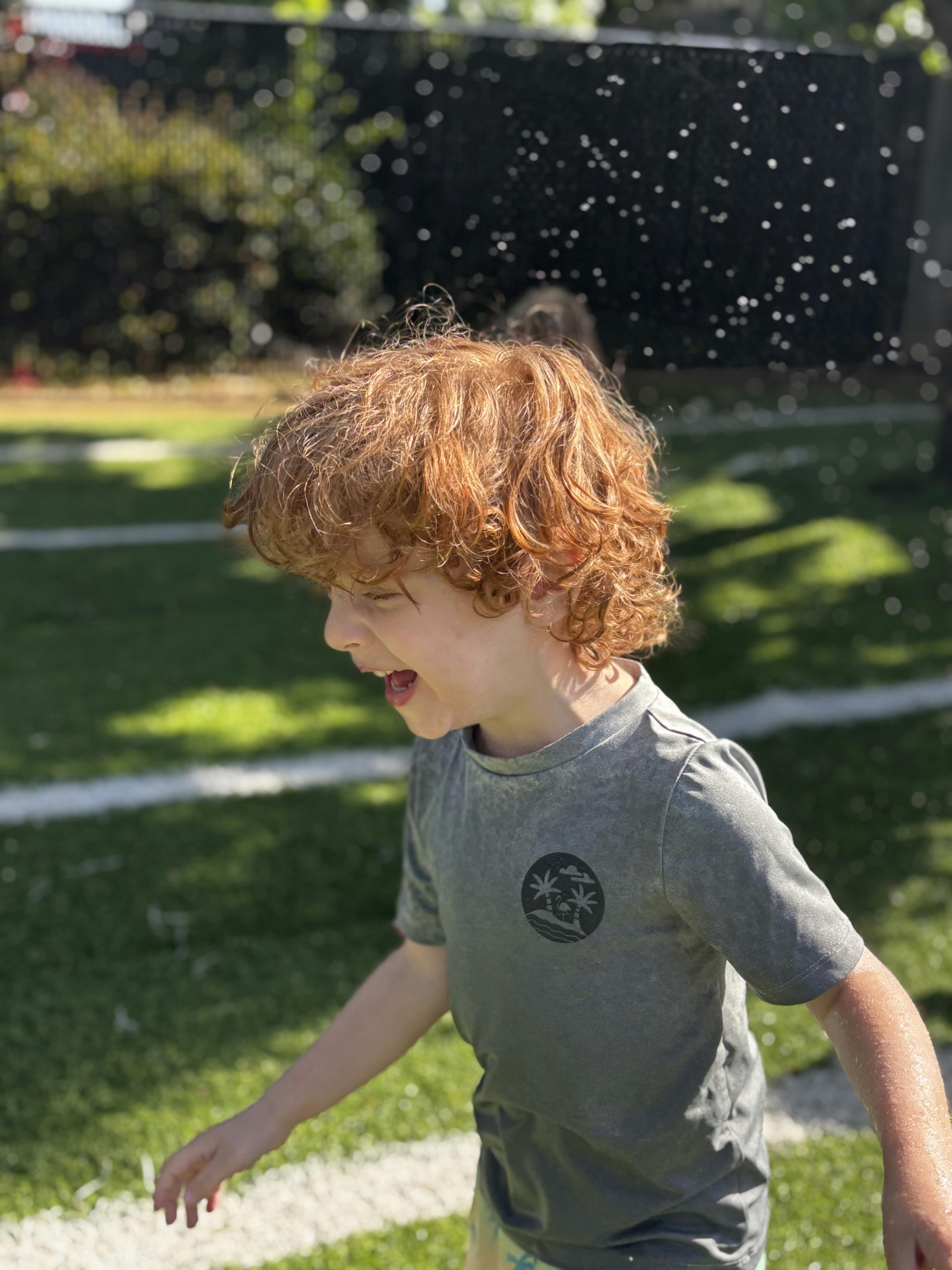 Child with red curly hair playing outdoors with water droplets
