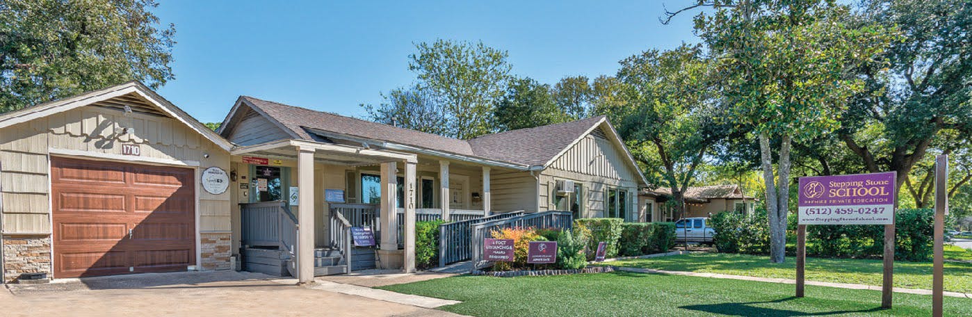Stepping Stone School building with front porch and small yard, purple business signs