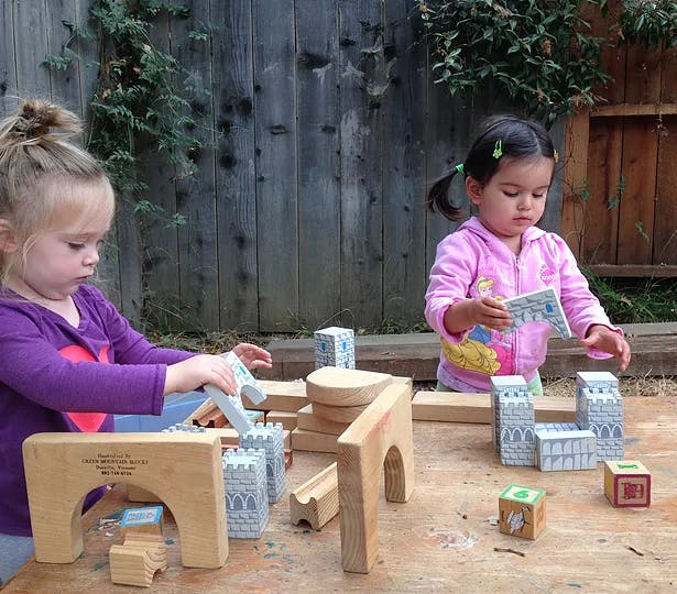 Two children playing with wooden and castle-themed blocks