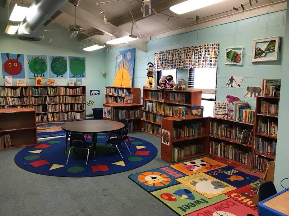 Children's library with bookshelves, a round table, and colorful rugs