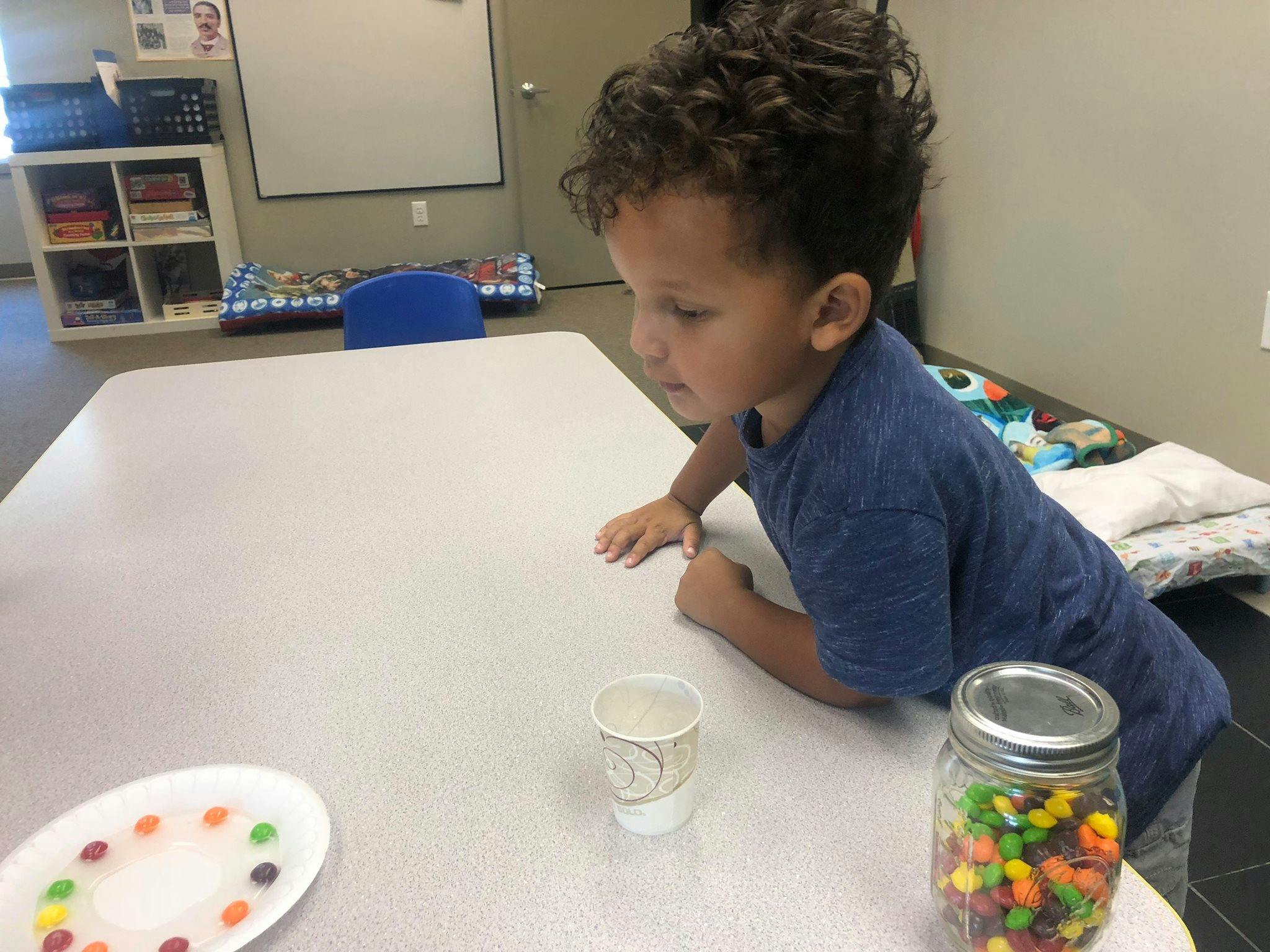 Child leaning on a table looking at a cup and jar of candy