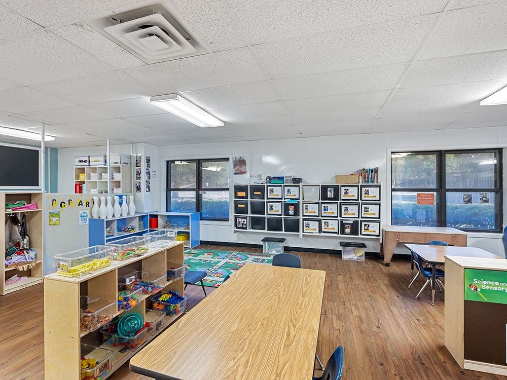 An empty classroom with tables, chairs, and shelves of toys