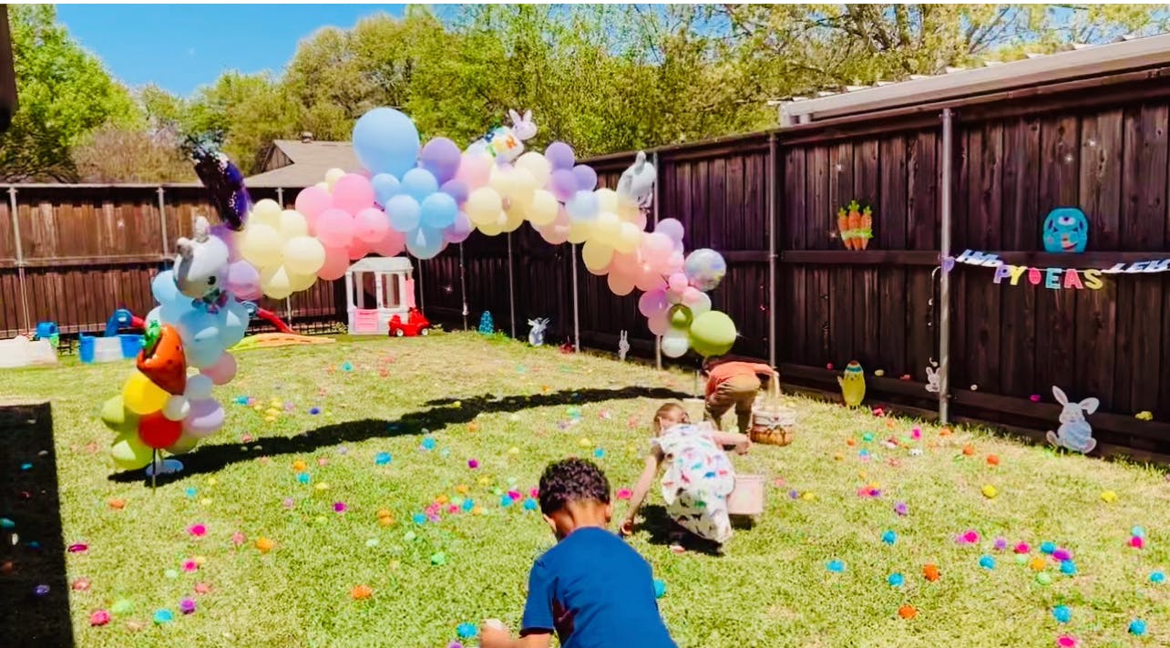 Children collecting eggs in a yard with a balloon arch