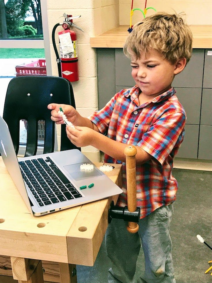 Child holding small objects over a laptop
