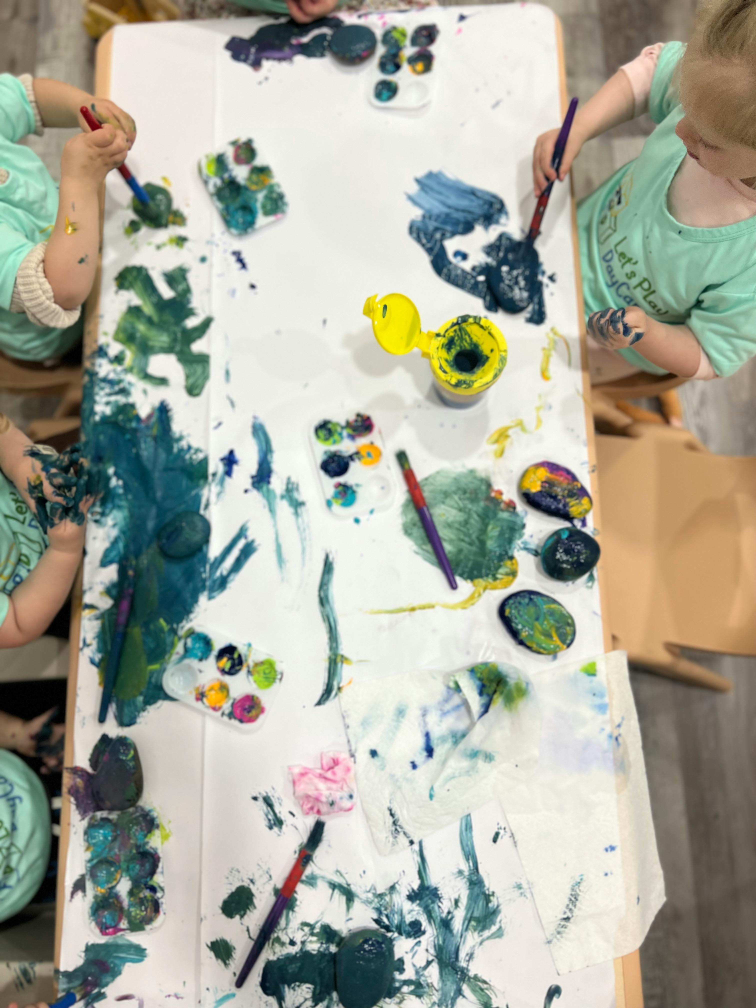 Two children painting on a table covered in paper and paint