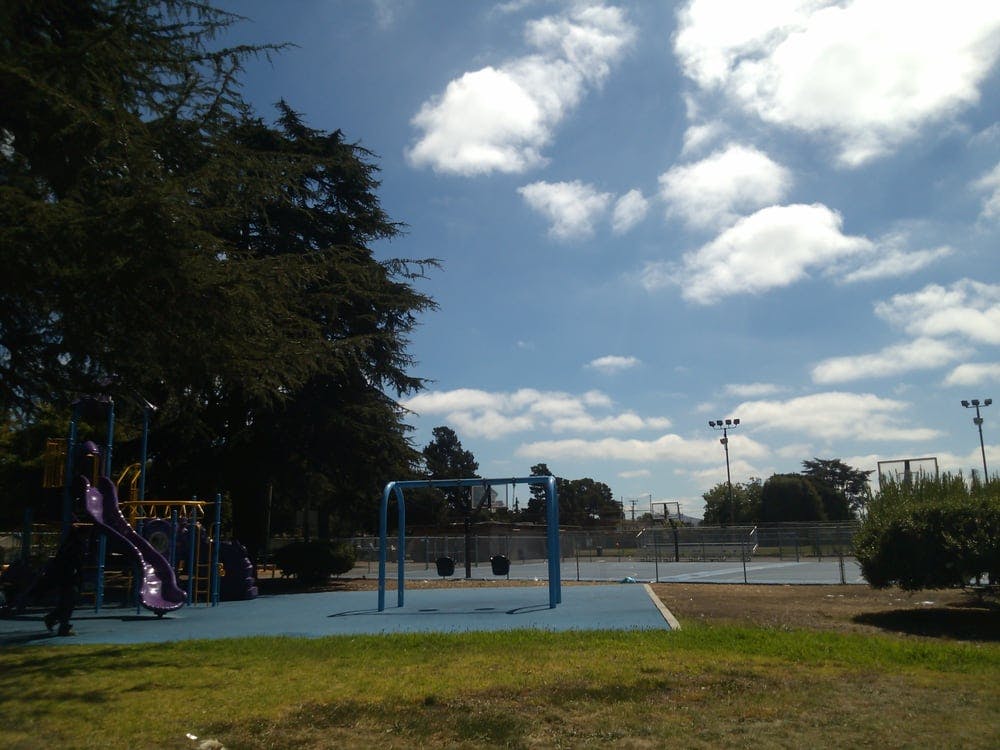 Playground with slide and swings next to a tennis court under a cloudy sky