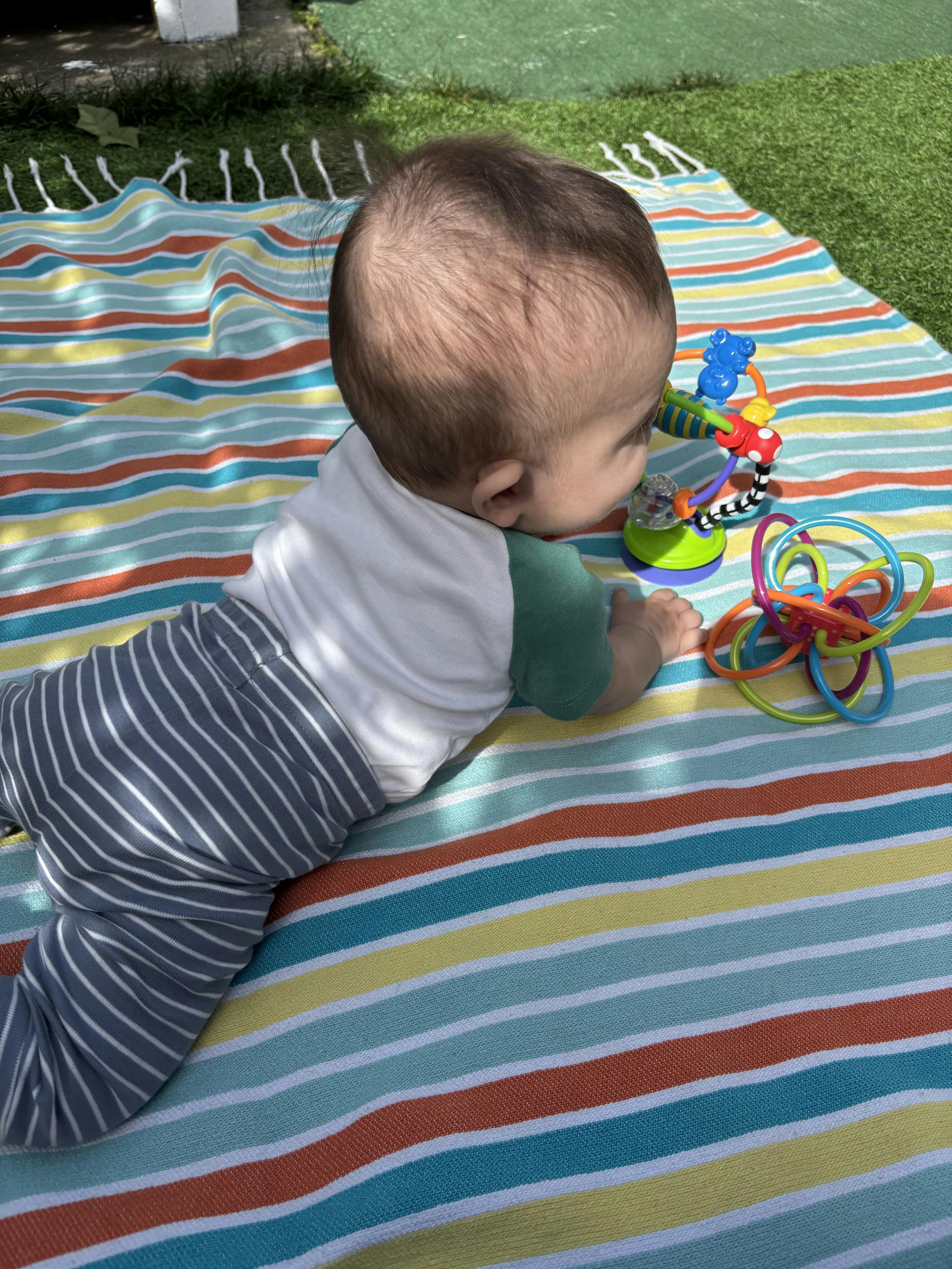 Child lying on a striped blanket, reaching for toys