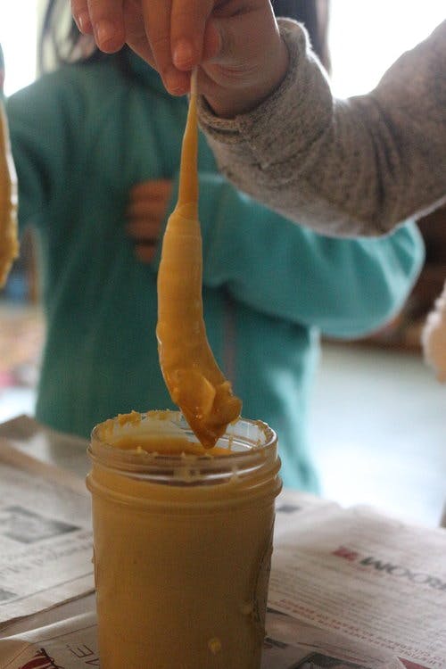 Person dipping a stick into a jar of peanut butter