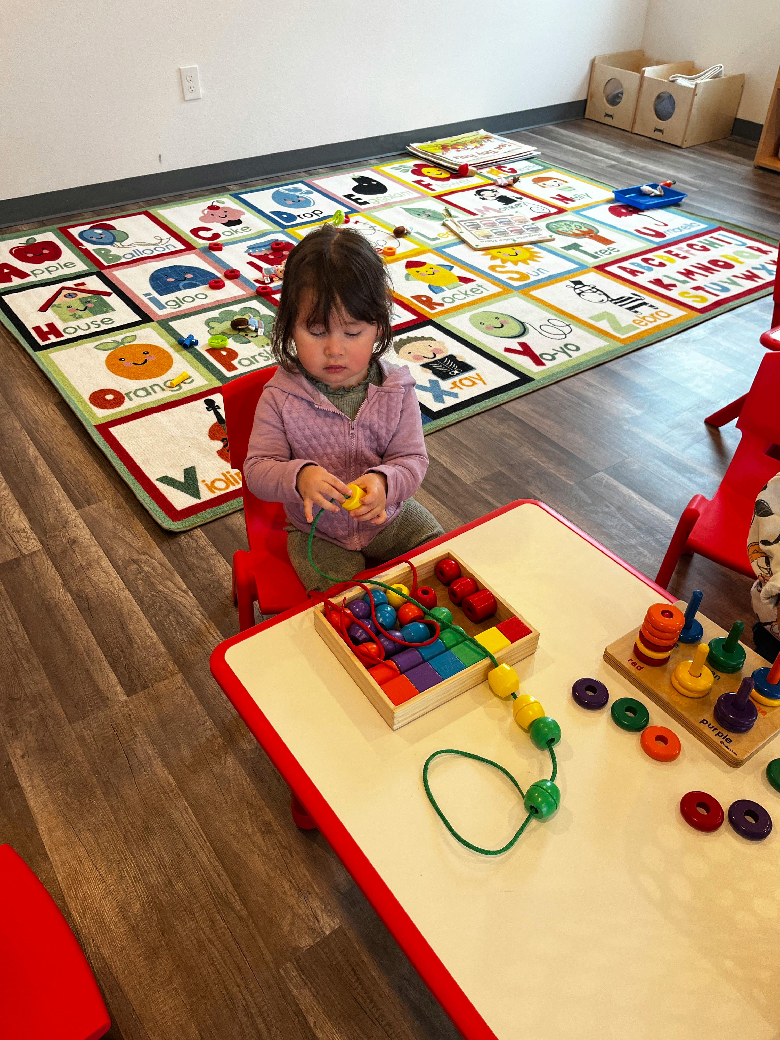 Child sitting at a table playing with colorful beads and toys