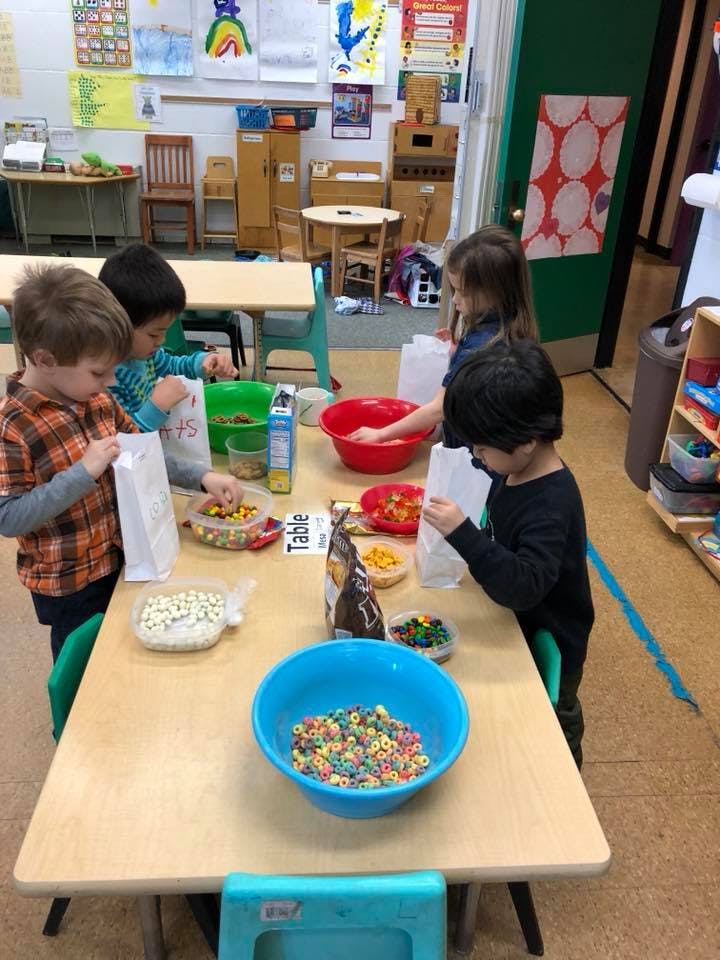 Children filling bags with snacks at a table in a classroom