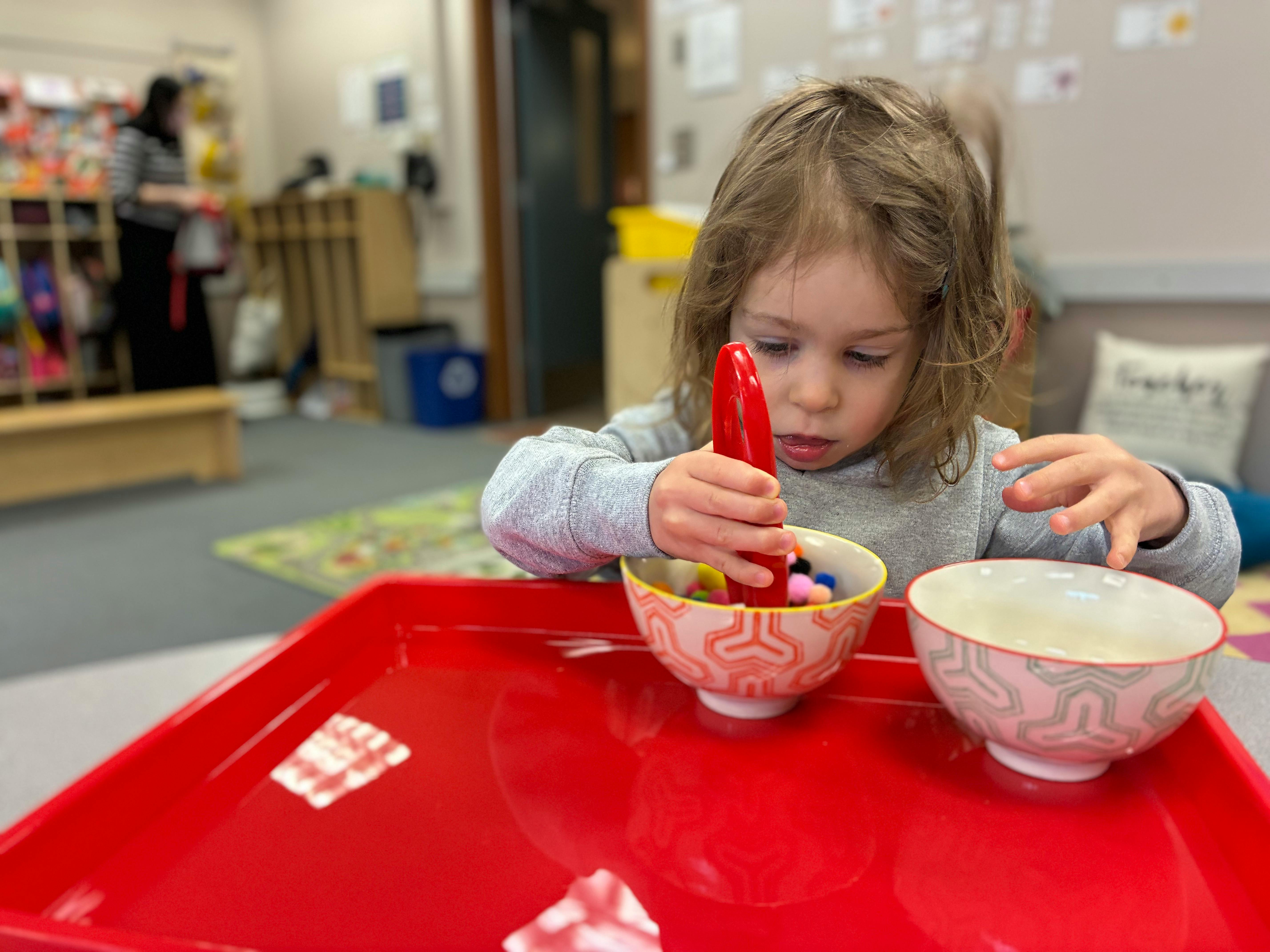 Child using tongs to move small objects from one bowl to another