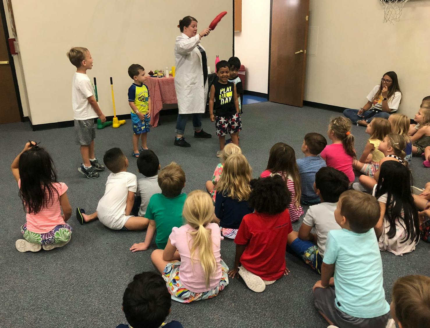Person in lab coat showing something to a group of children