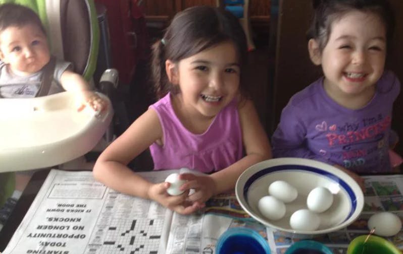 Three children at a table with eggs and newspaper