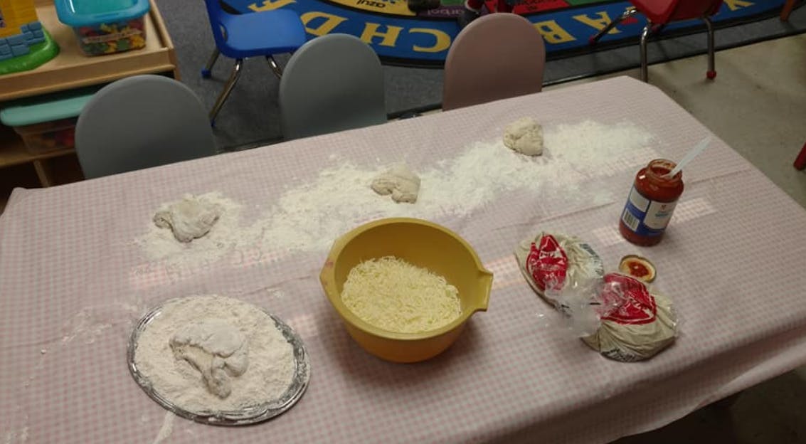 Table with flour, a bowl of cornmeal, and a jar of sauce